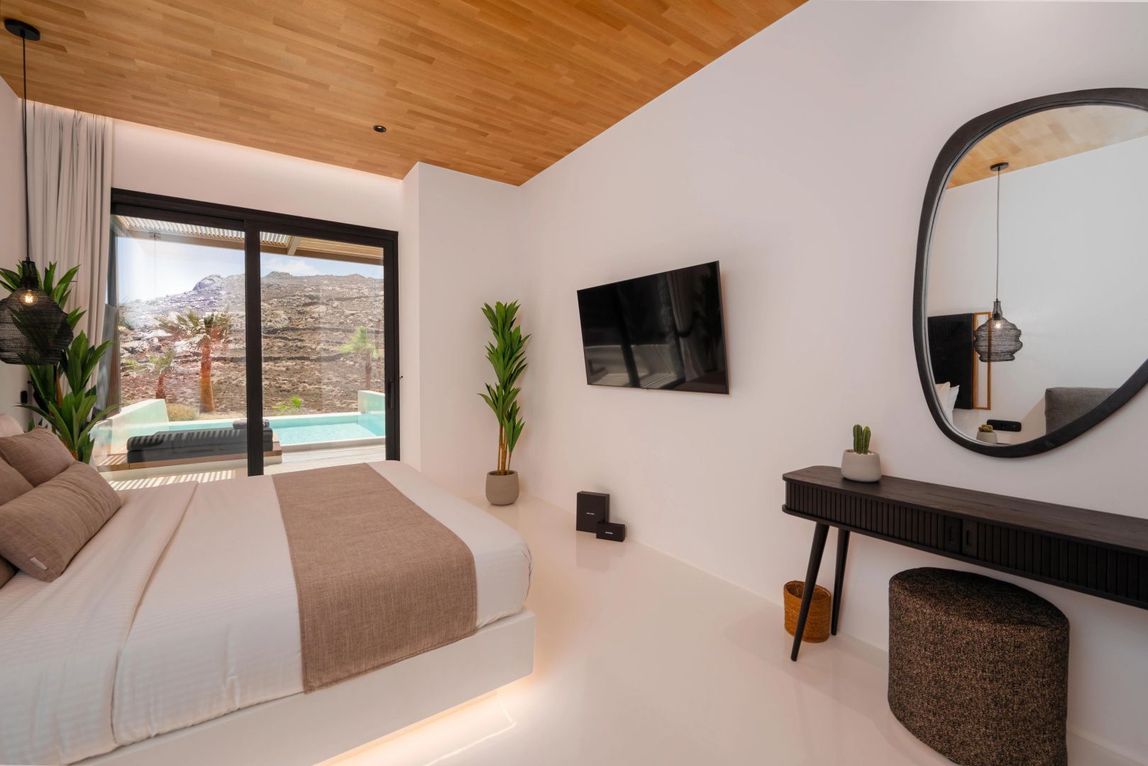 Schlafzimmer mit Doppelbett, Holzdecke, Fernseher und Blick durch die Glasschiebetür zum Pool.