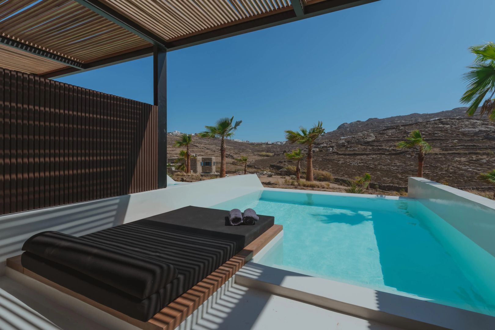 Sonnenterrasse mit privatem Pool, Liegebett und Blick auf hügelige Landschaft.