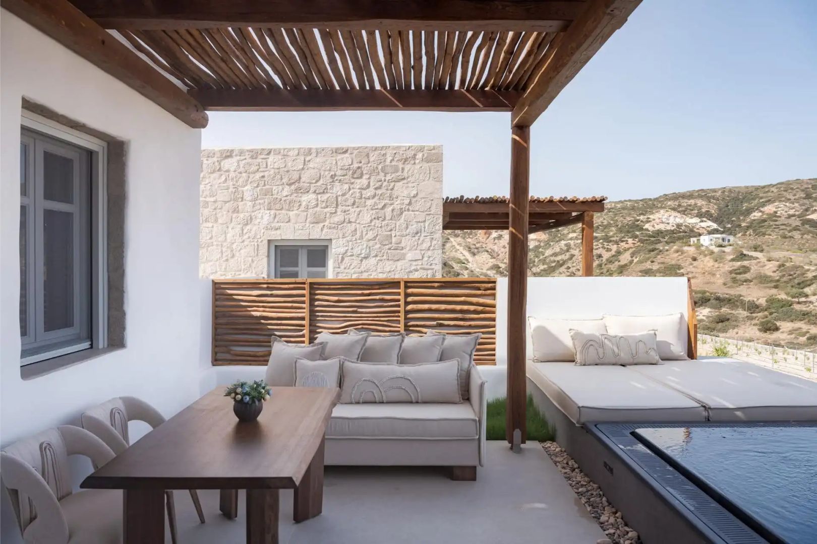 Überdachte Terrasse mit Esstisch aus Holz, hellem Polstersofa und Blick auf die Landschaft.