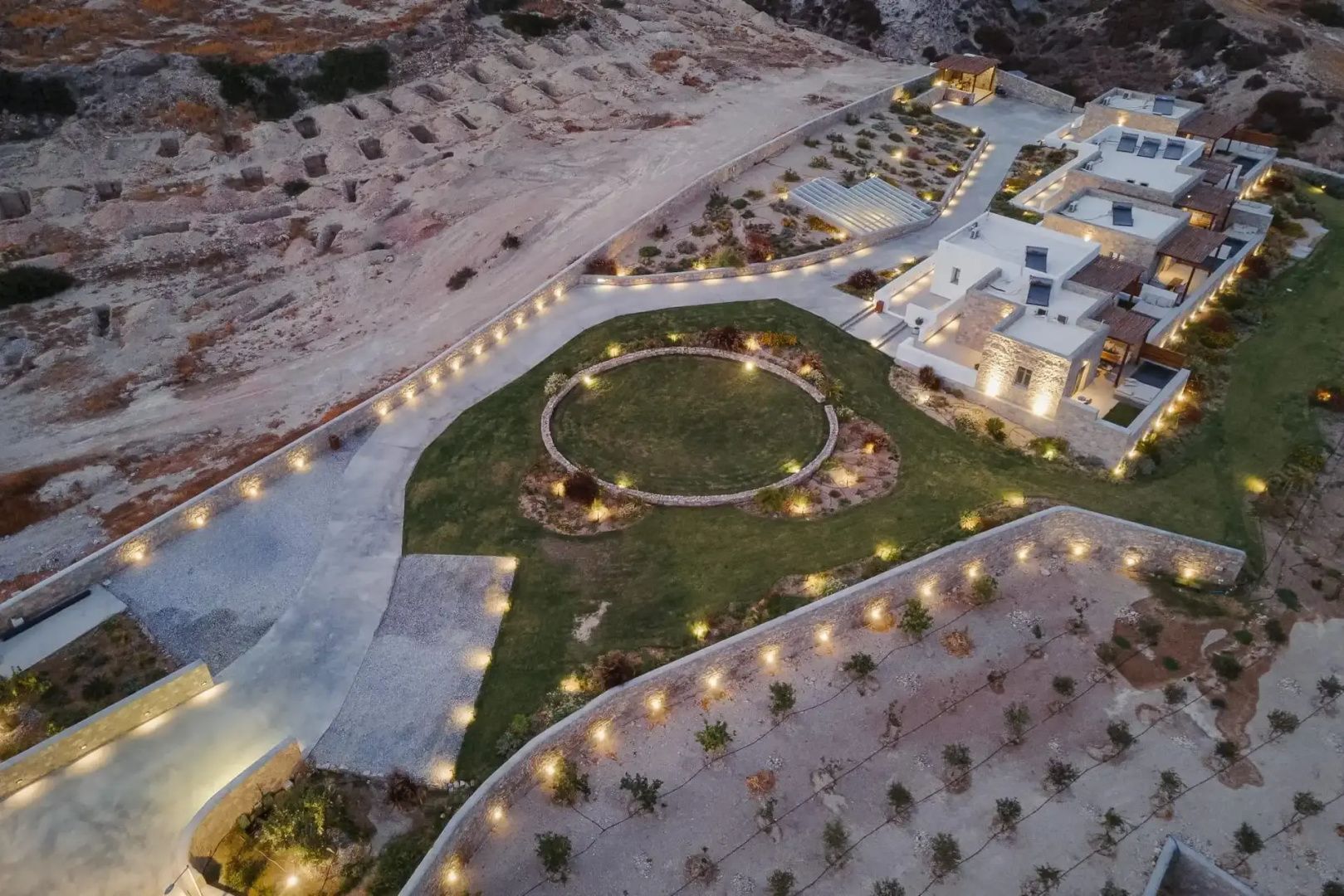Luftaufnahme der Hotelanlage mit beleuchteten Wegen, Kreisrasen und umliegender Landschaft.