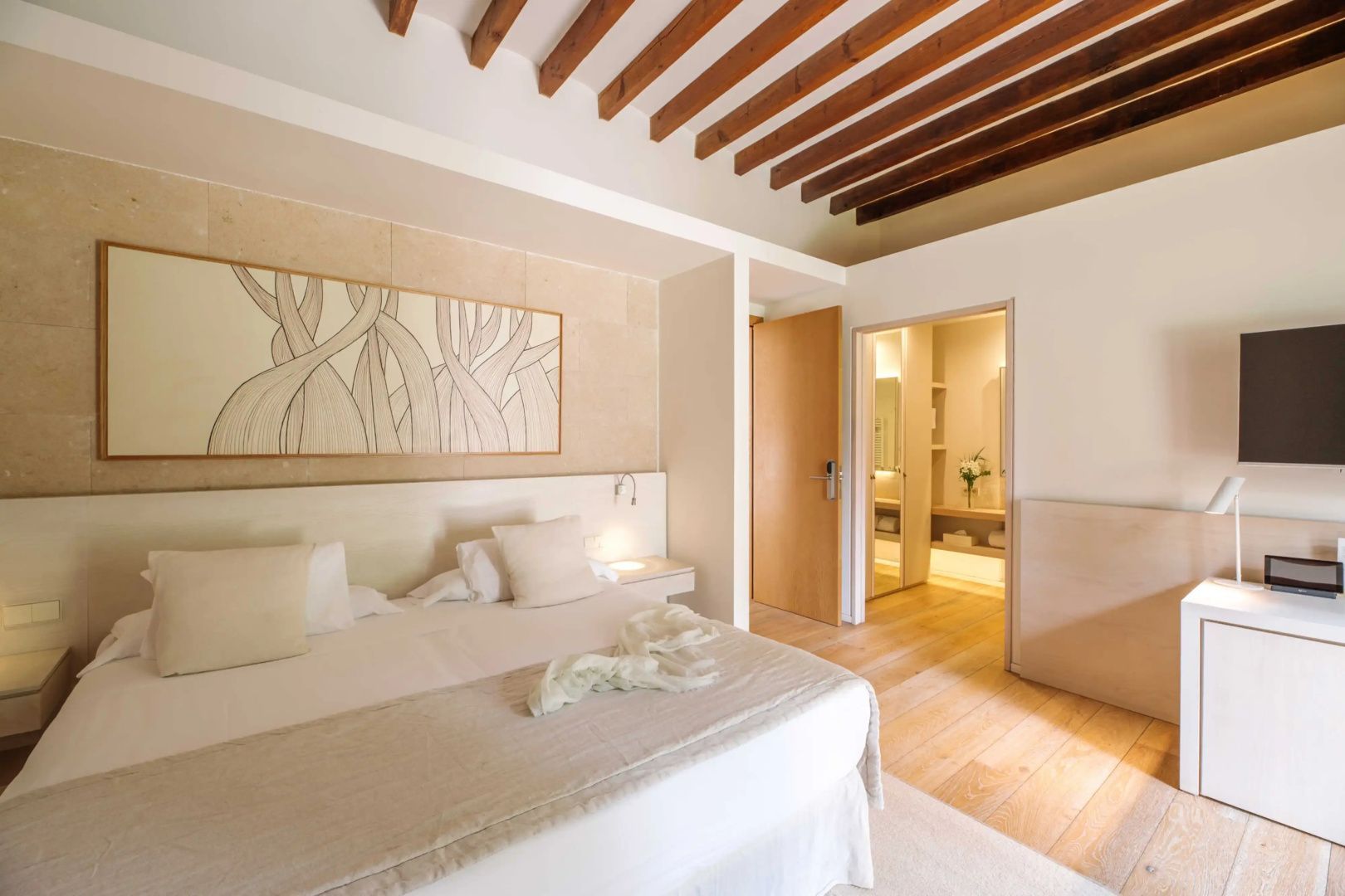 Doppelbett mit hellem Kopfteil, Holzdecke und Wandbild im Hotelzimmer.