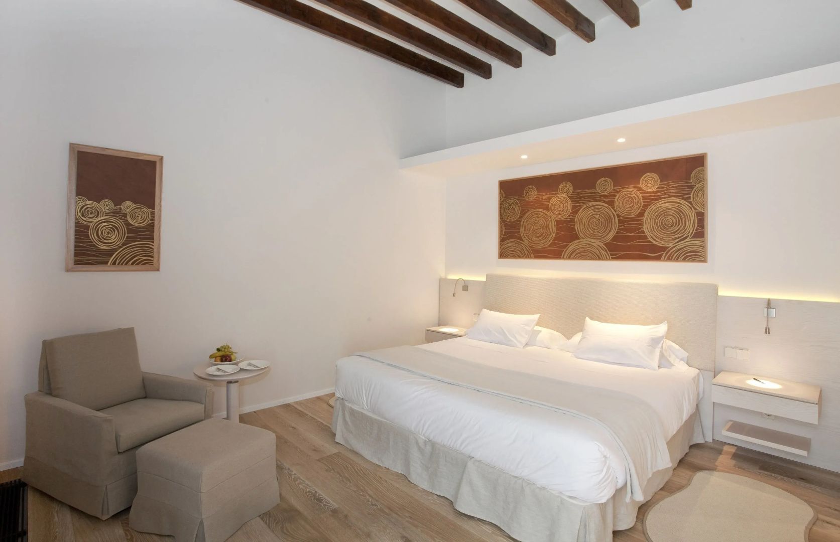 Helles Hotelzimmer mit einem Doppelbett, sichtbaren Holzbalken an der Decke und Sitzgelegenheiten.