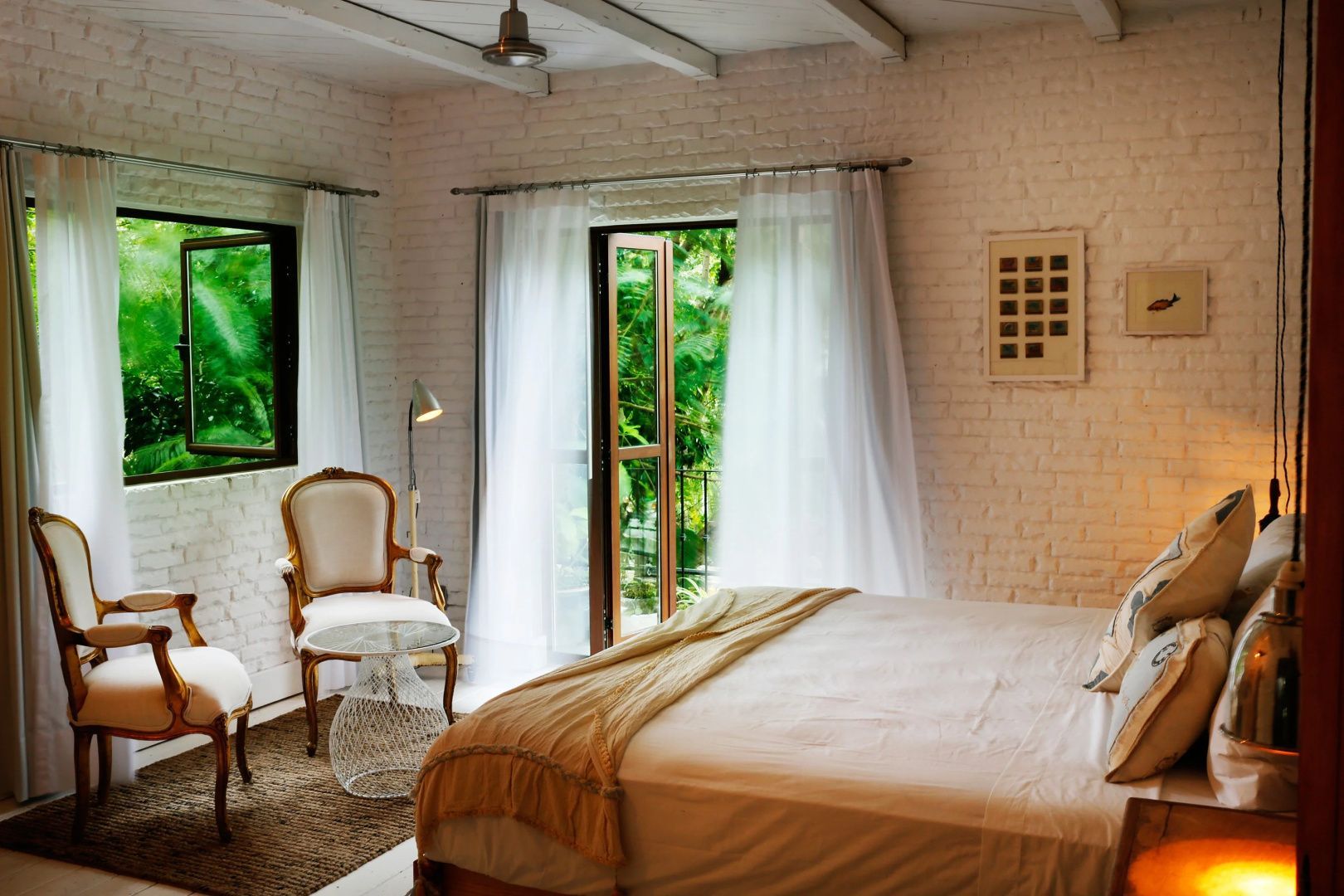 Hotelzimmer mit weißer Ziegelwand, Sessel und Balkontür ins Grüne.
