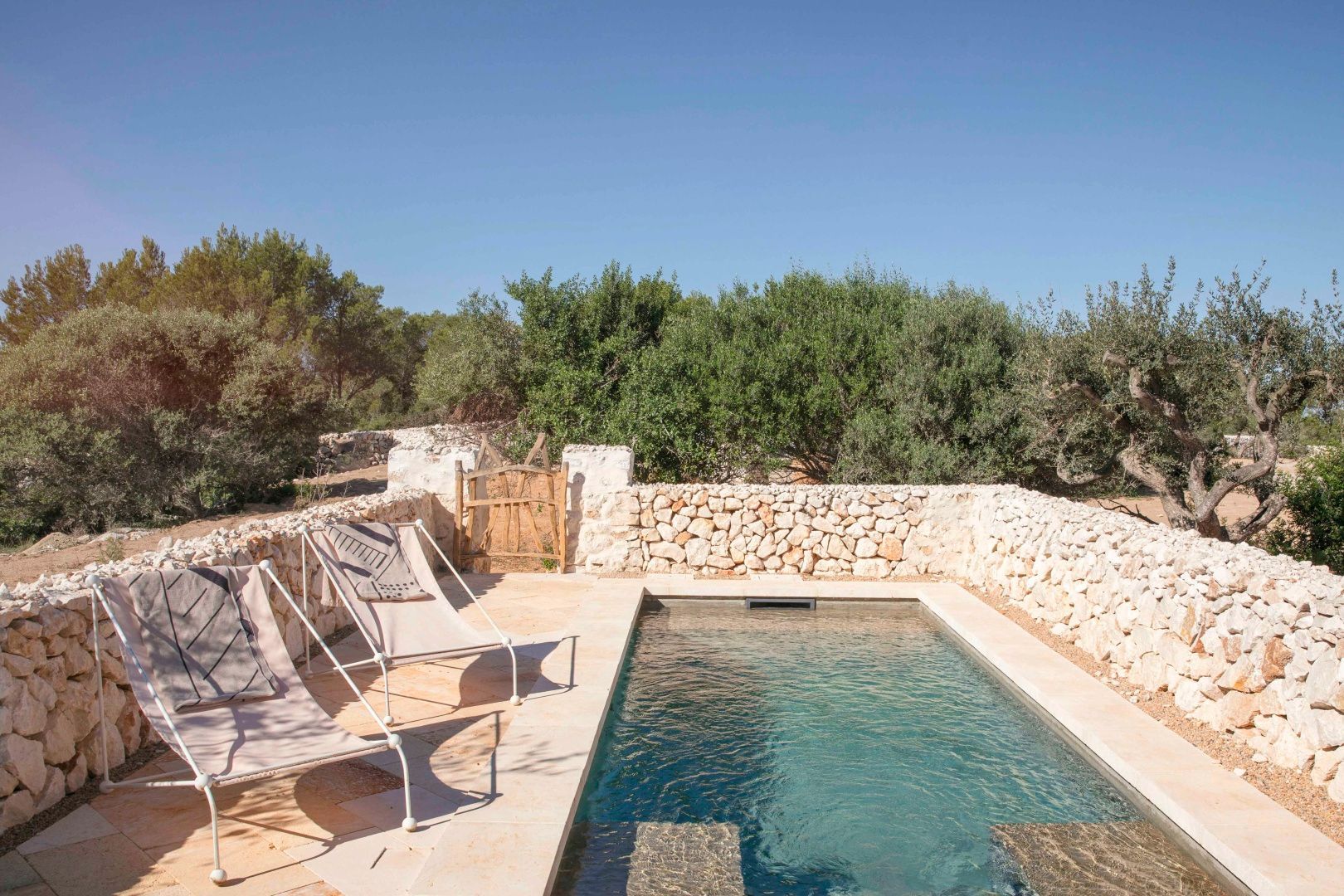 Ein kleiner Swimmingpool auf einer Terrasse mit Natursteinmauer und zwei Liegestühlen.
