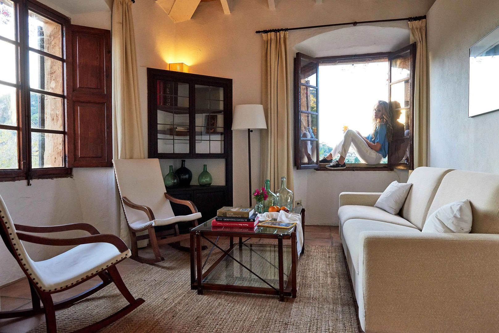 Wohnbereich einer Suite mit Sofa, Schaukelstühlen und einer Person am geöffneten Fenster.
