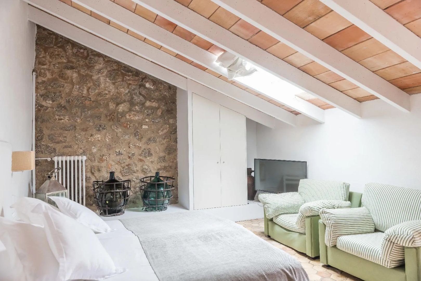 Schlafzimmer unter der Dachschräge mit Natursteinwand, grünen Sesseln und Doppelbett.