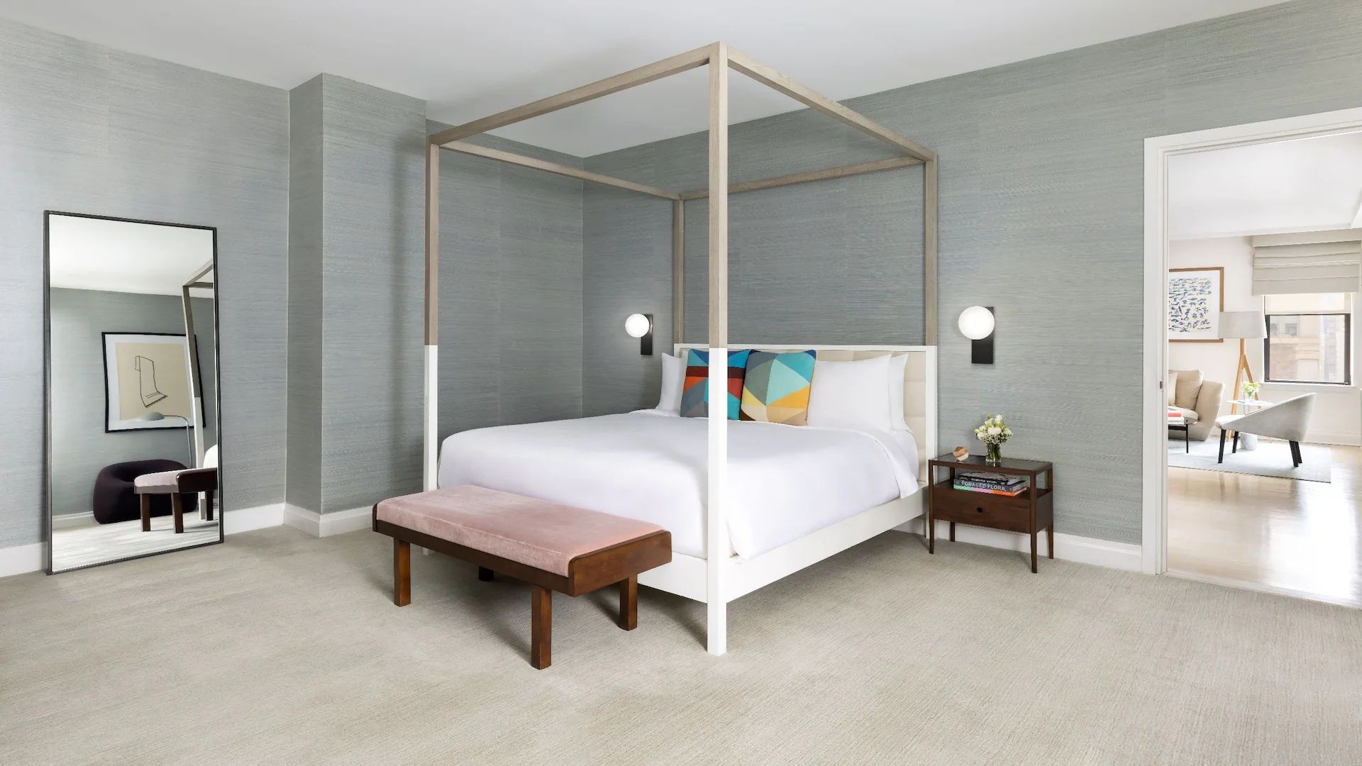Doppelzimmer mit einem modernen Himmelbett aus Holz, einer rosa Bank und grauer Tapete.