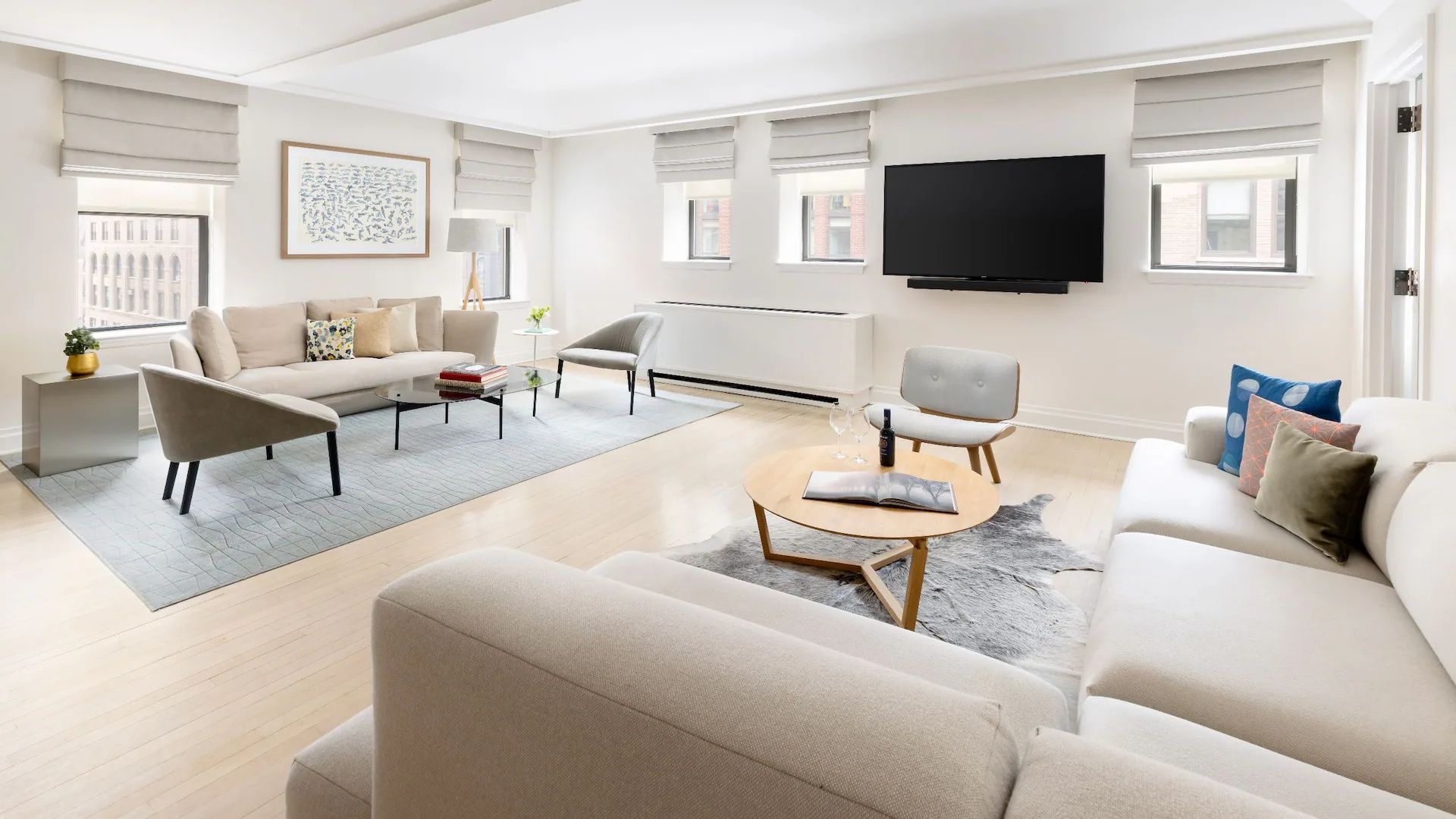 Lichtdurchfluteter Wohnbereich einer Suite mit großem Fernseher, Sofa und hellem Holzboden.