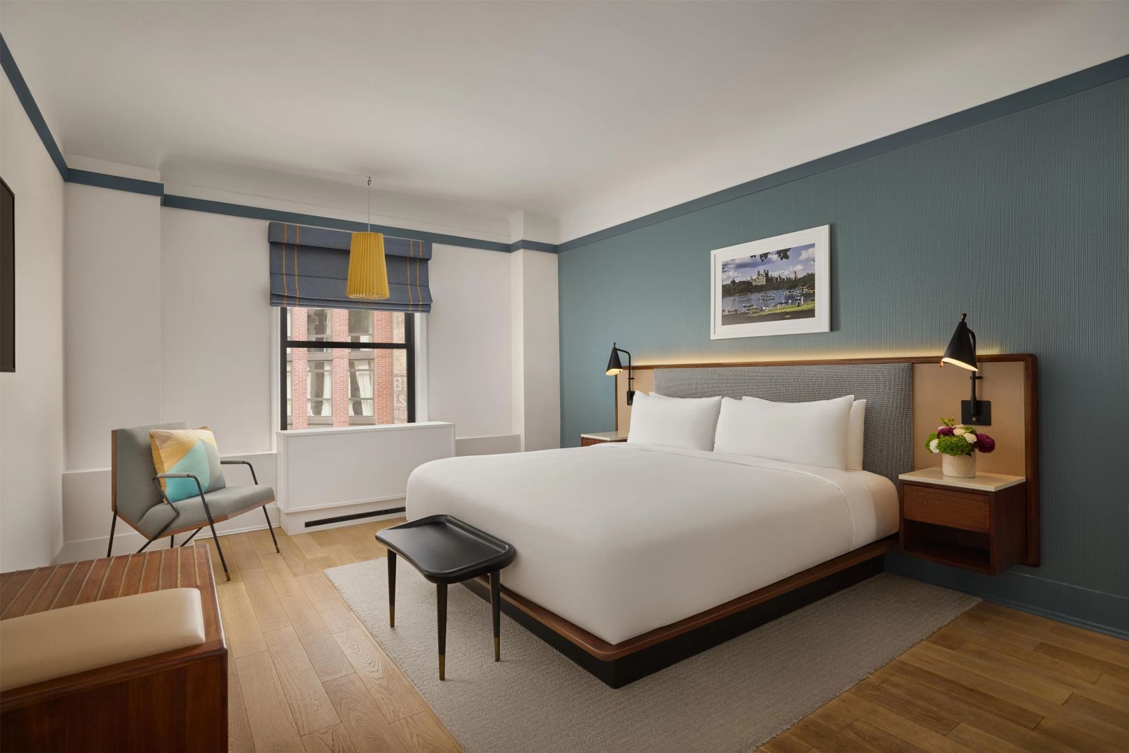 Hotelzimmer mit großem Doppelbett, blau akzentuierter Wand, Parkettboden und Fenster.