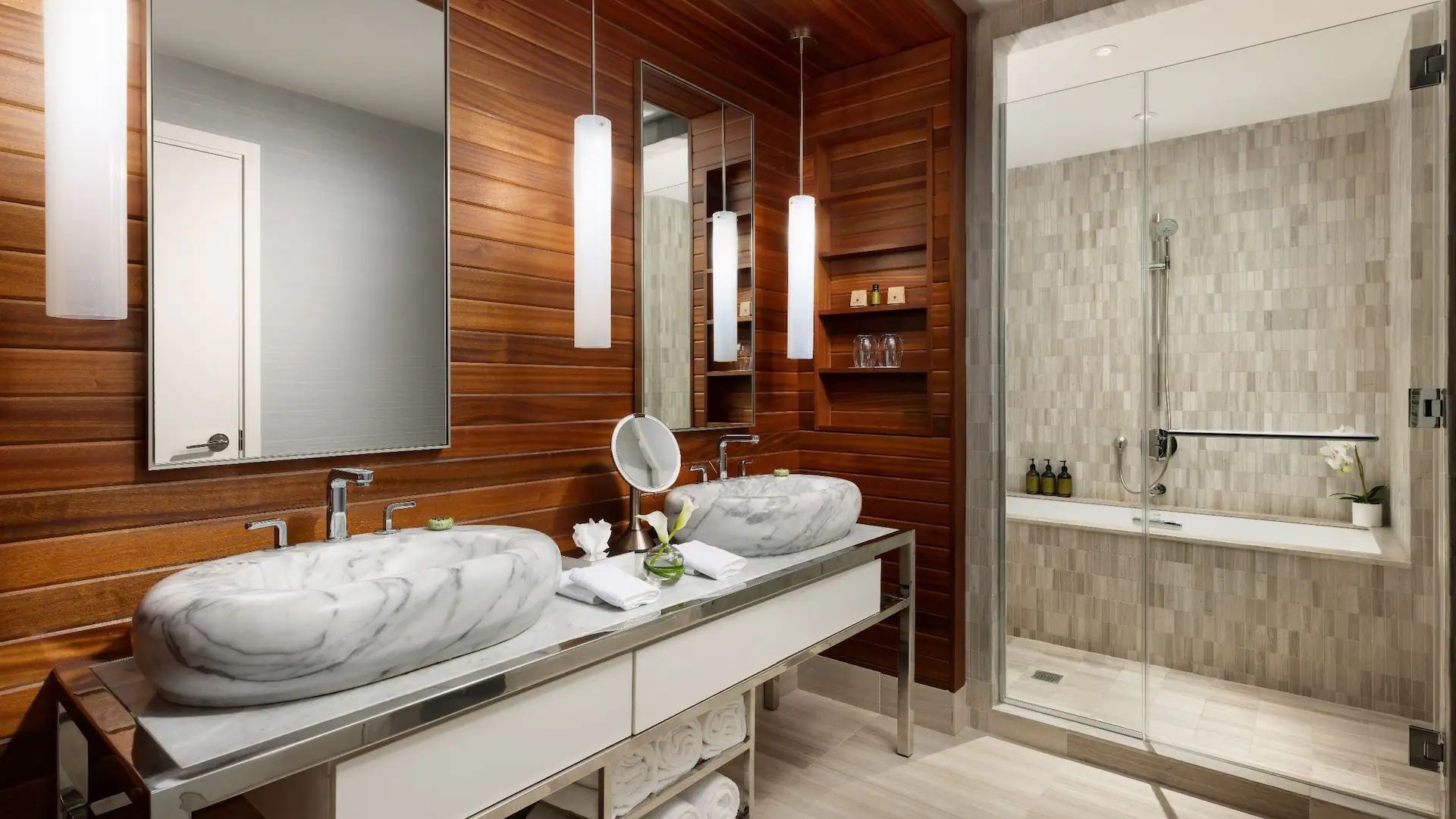 Badezimmer mit Doppelwaschtisch aus Marmor, Holzverkleidung und hängenden Zylinderlampen.
