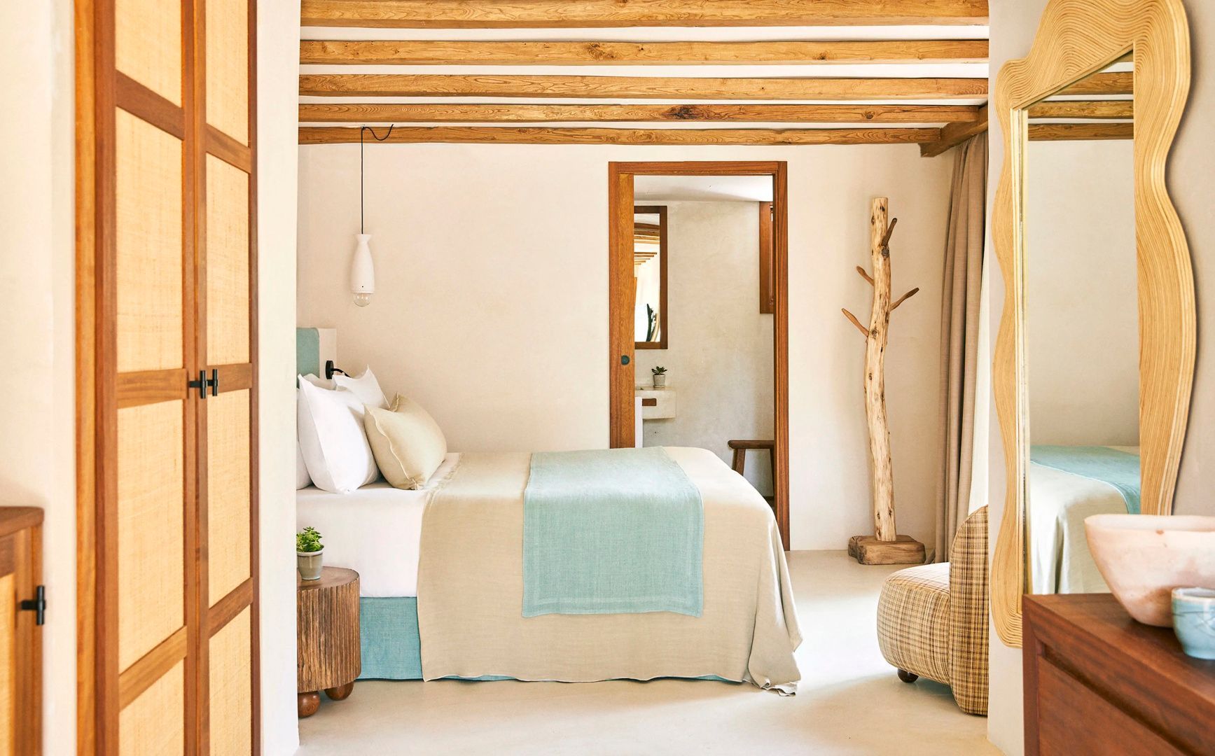 Helles Hotelzimmer mit Doppelbett, Holzbalkendecke und Blick ins angrenzende Badezimmer.
