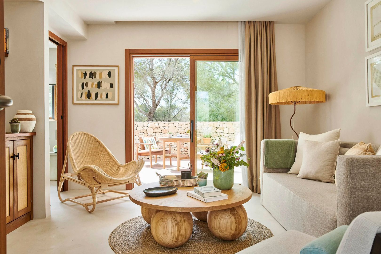 Wohnzimmer mit Flechtstuhl, Holztisch und großer Glastür zur angrenzenden Terrasse.