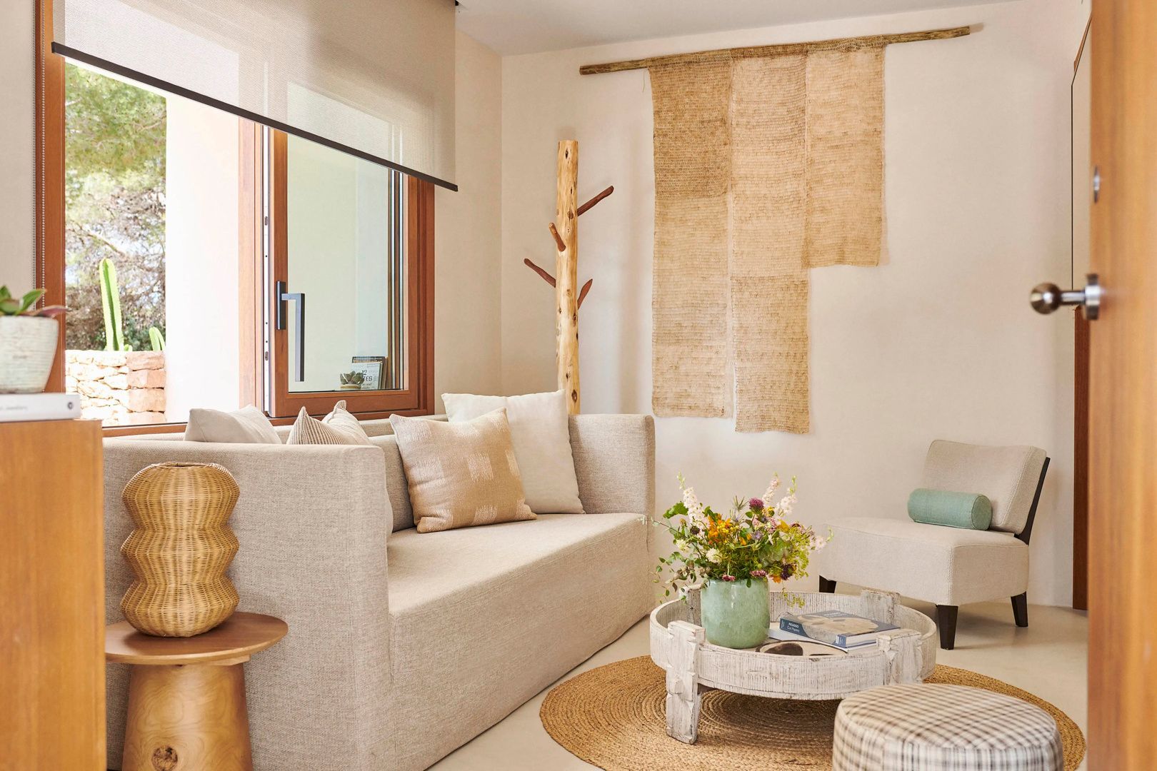 Helles Wohnzimmer mit beigem Sofa, Holztisch, Blumentopf und Wandteppich aus Naturfasern.