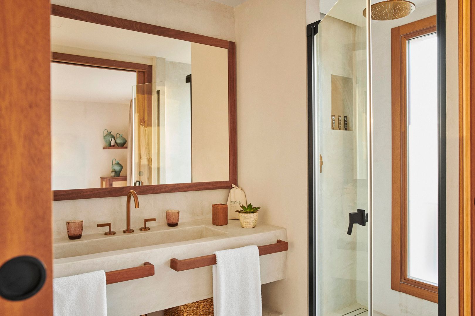 Badezimmer mit beigefarbenem Waschtisch, großem Holzspiegel und gläserner Dusche.