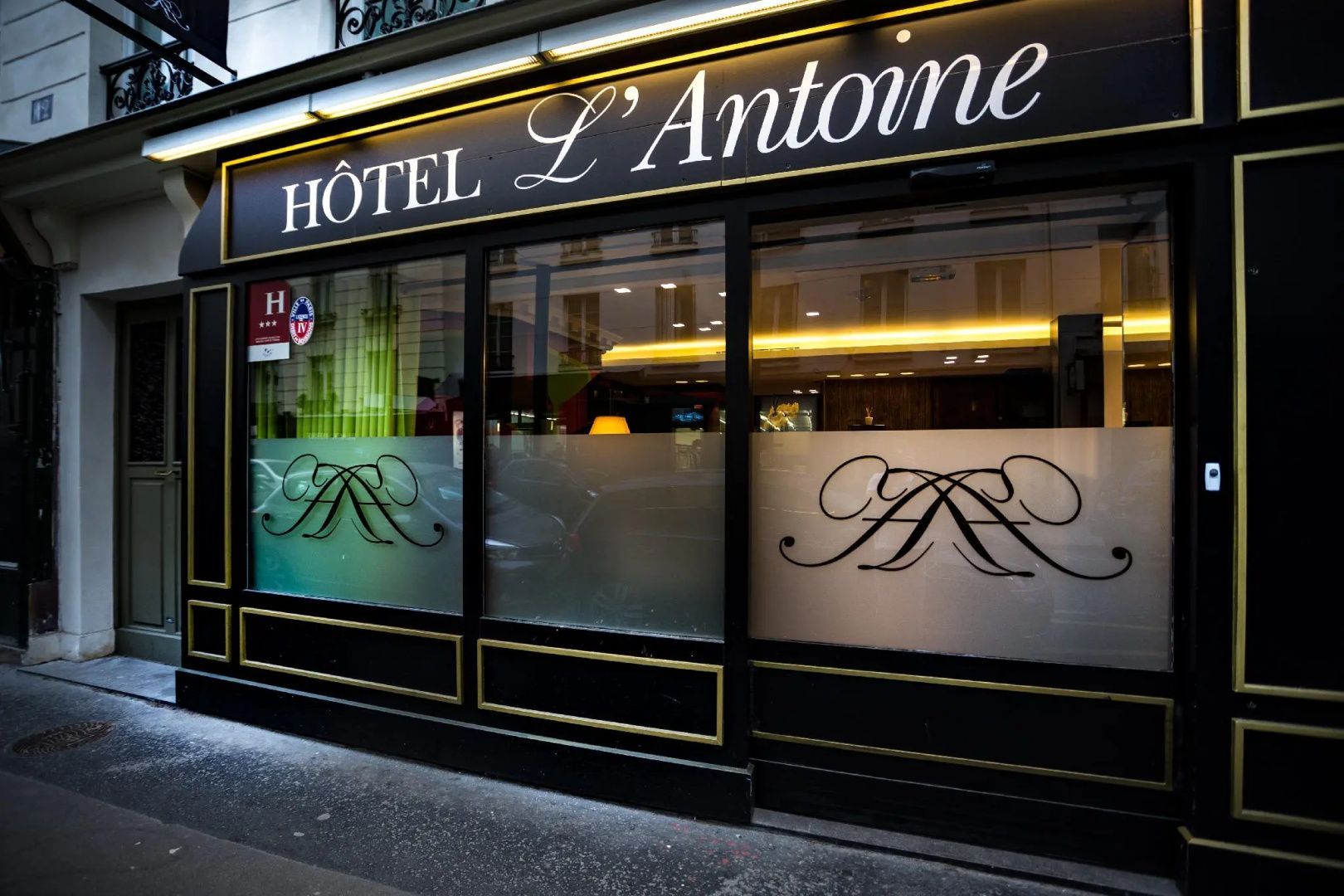 Dunkle Fassade des Hôtel L'Antoine mit goldener Schrift und matten Fensterscheiben.