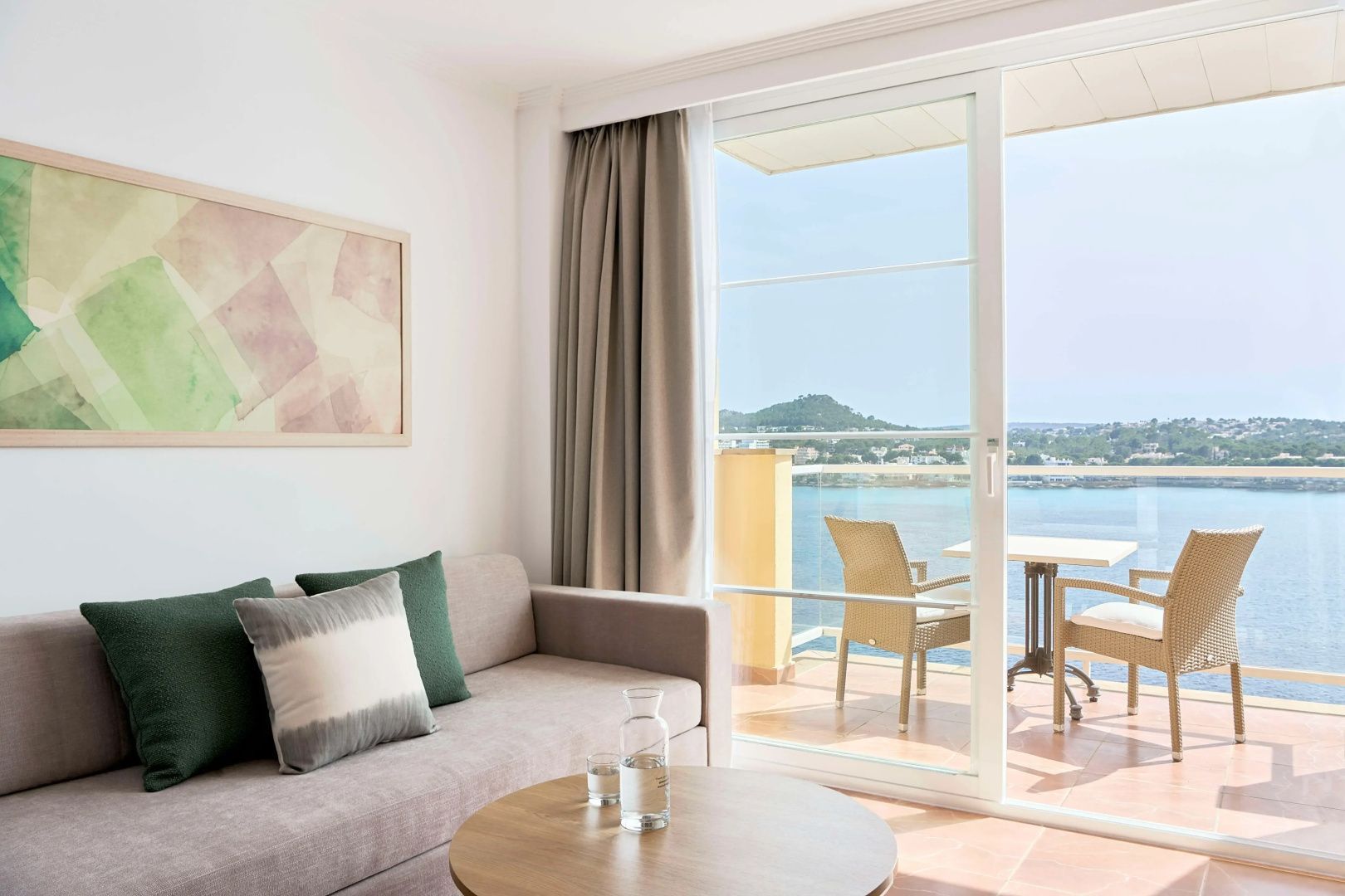 Blick durch die große Glasfront der Suite auf den Balkon und das dahinter liegende Meer.