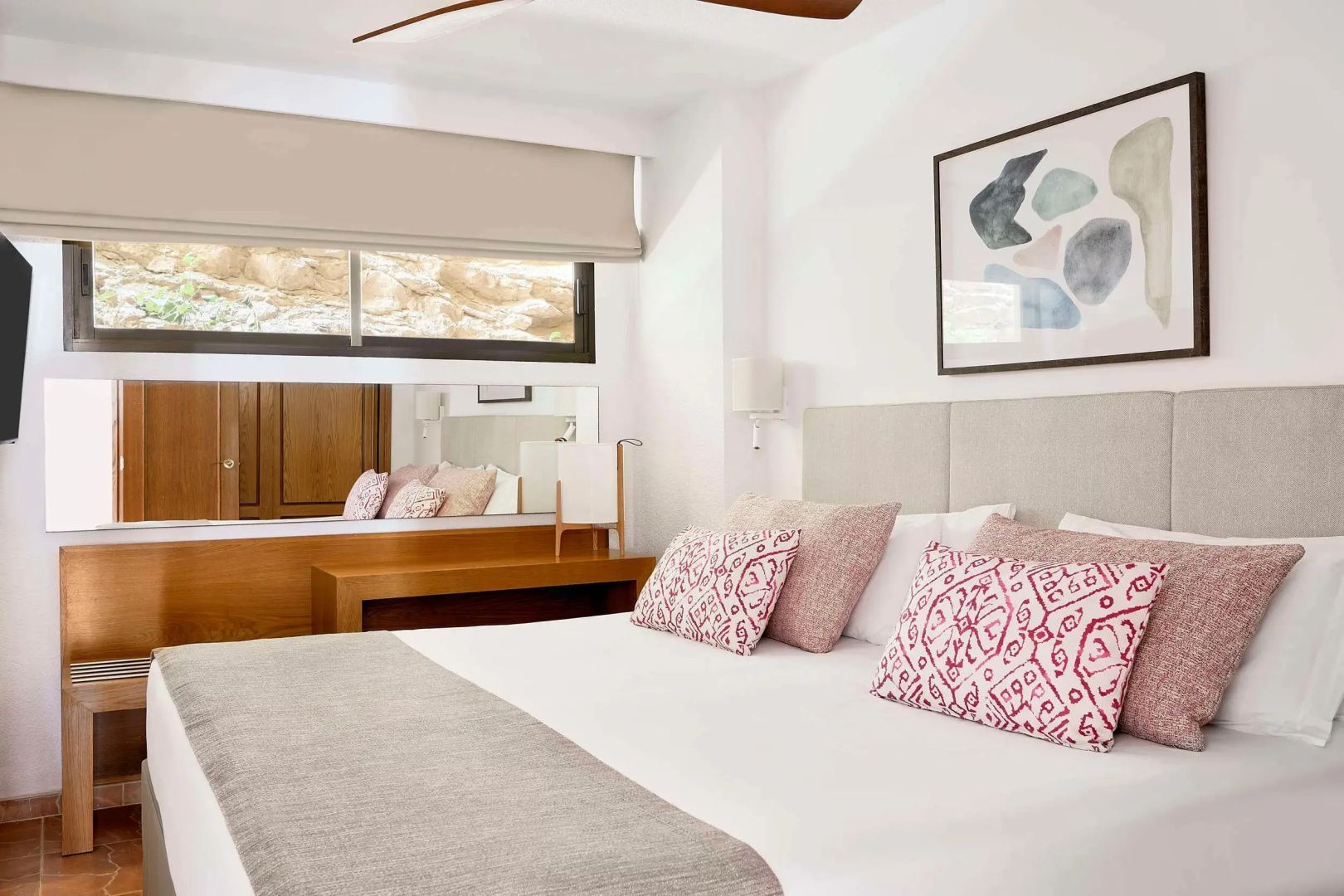 Helles Schlafzimmer mit Doppelbett, gemusterten Kissen und einem Bild an der Wand.