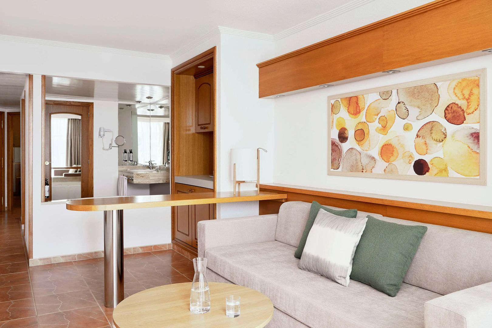 Sitzbereich einer Suite mit hellem Sofa, buntem Wandbild und Holzelementen.