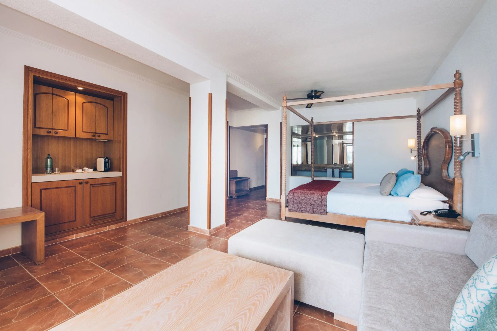 Geräumiges Hotelzimmer mit Fliesenboden, Holzmöbeln und einem Himmelbett im Hintergrund.