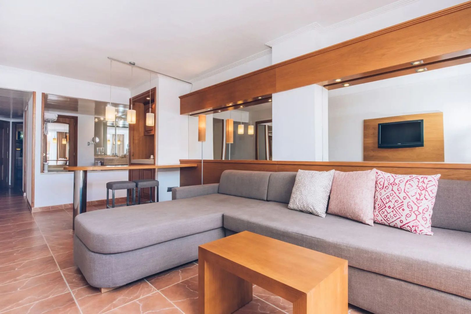Geräumiger Wohnbereich einer Suite mit Ecksofa, Holztisch und großem Wandspiegel.