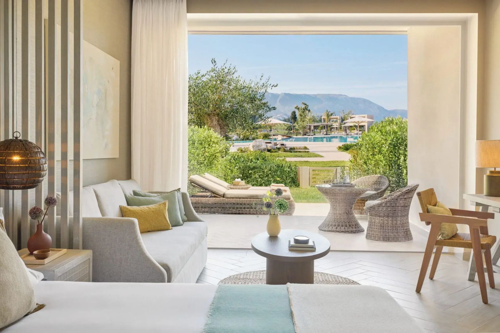 Helles Hotelzimmer mit Sofa, Couchtisch und Ausblick auf die Terrasse sowie den Garten.