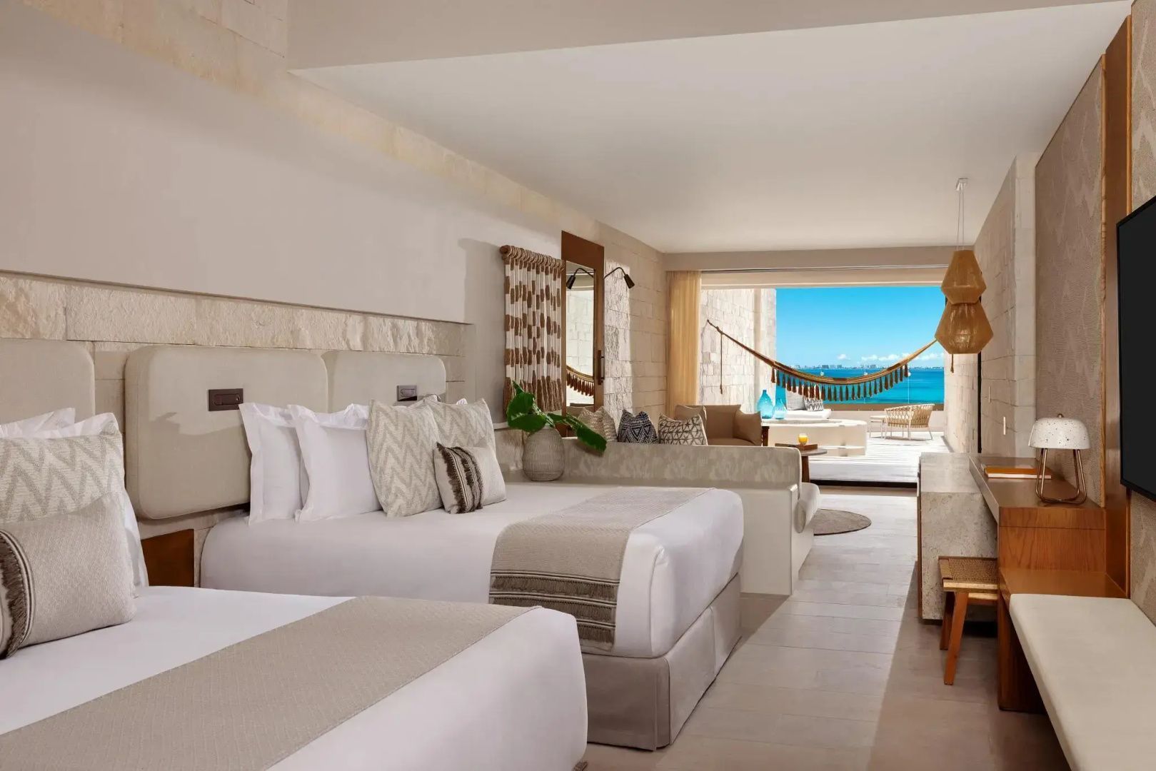 Helles Hotelzimmer mit zwei Betten, Sitzbereich und Balkon mit Blick auf das blaue Meer.