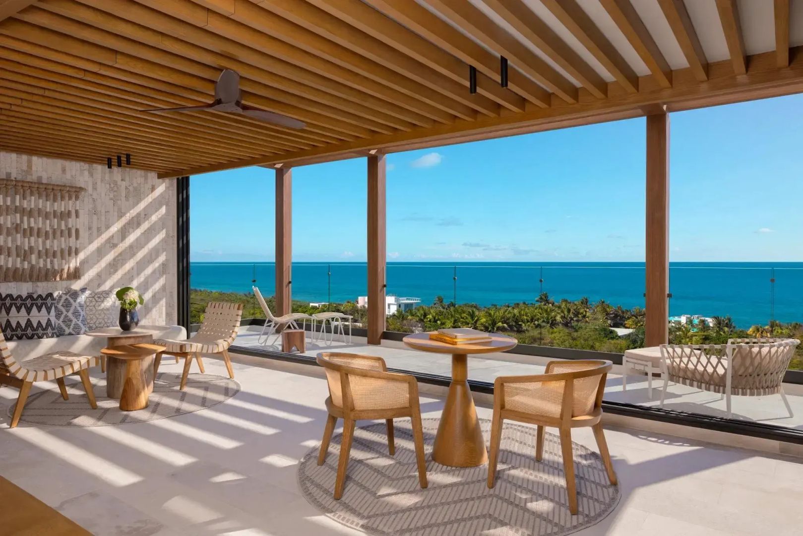 Überdachte Terrasse mit Holzstühlen, einem kleinen Tisch und Blick auf das Meer.