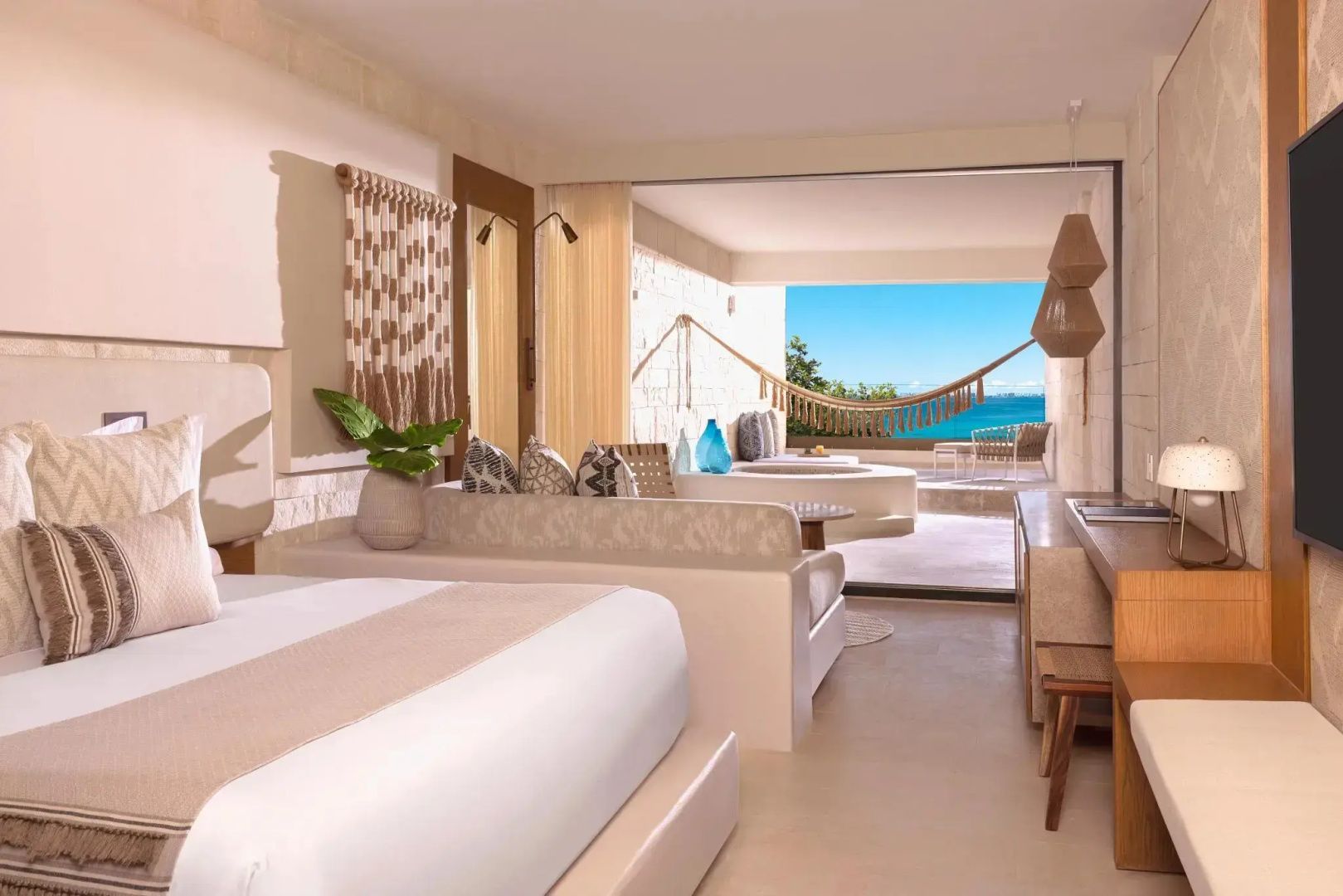 Helles Hotelzimmer mit Doppelbett, Couch und Zugang zur Terrasse mit Hängematte und Meerblick.