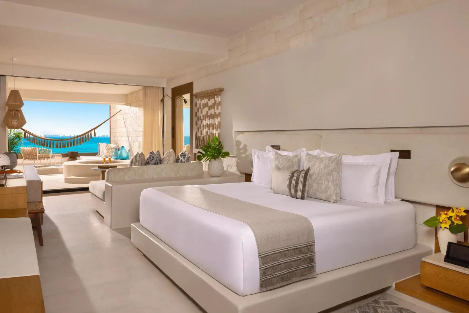 Helles Hotelzimmer mit großem Doppelbett, Sitzbereich und Balkon mit Blick auf das blaue Meer.