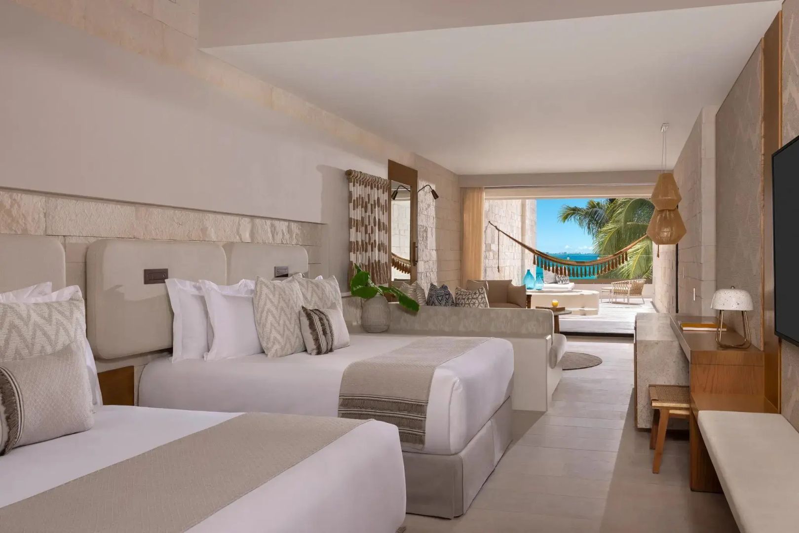 Hotelzimmer mit zwei Doppelbetten, hellem Interieur und Balkon mit Blick auf das Meer.