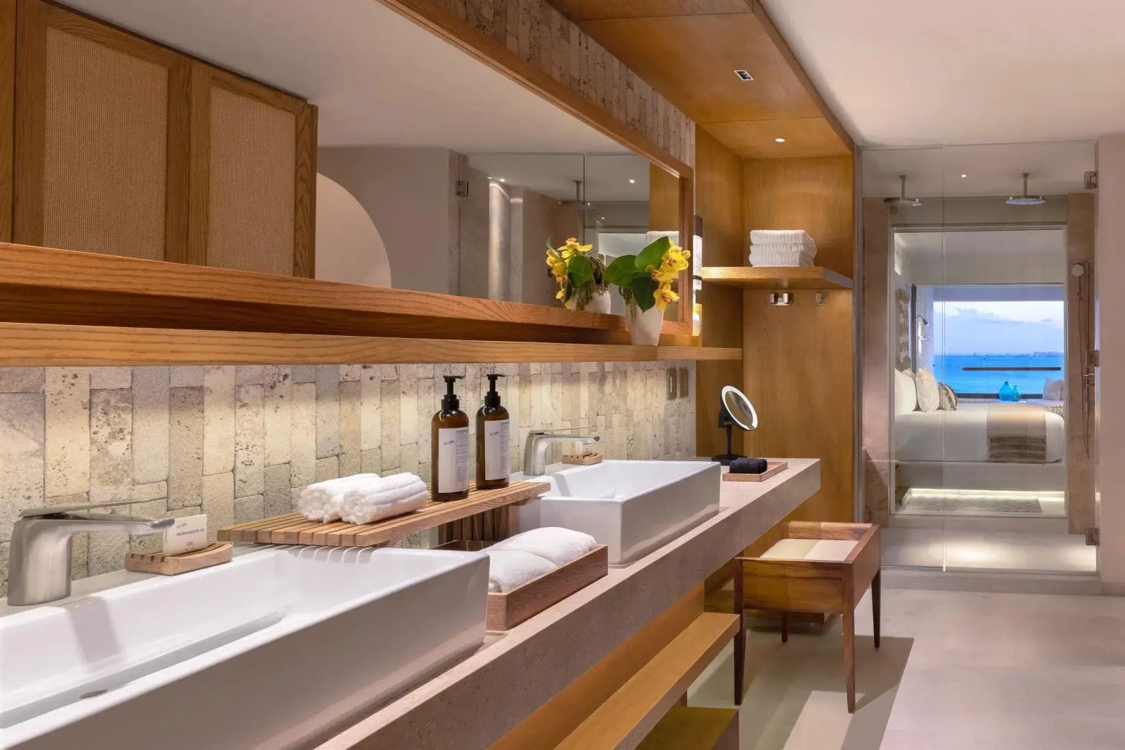 Badezimmer im Hotel mit zwei modernen Waschbecken, Holzregalen und einem großen Wandspiegel.