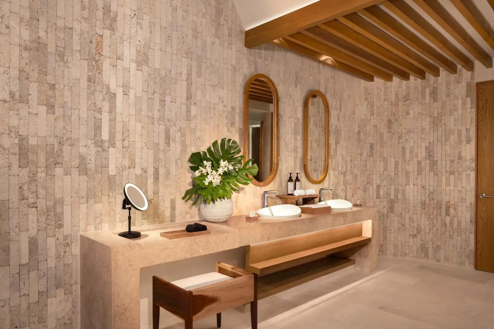 Waschtisch im Badezimmer mit zwei Waschbecken, zwei ovalen Spiegeln und Steinwand.