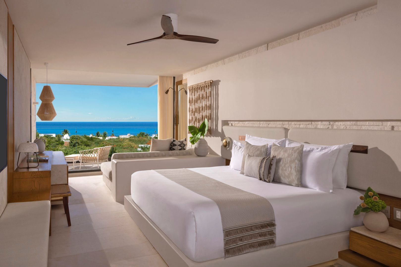 Hell eingerichtetes Schlafzimmer mit Doppelbett und Ausblick auf das Meer.