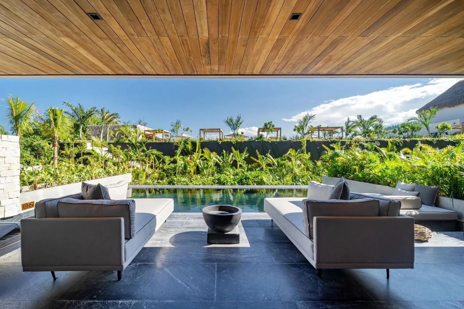Überdachte Terrasse mit Sitzmöbeln und Blick auf einen privaten Pool im Grünen.