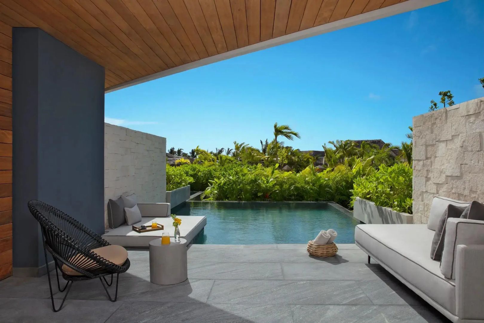 Überdachte Terrasse mit kleinem Pool, Liegemöglichkeiten und Blick auf tropische Pflanzen.