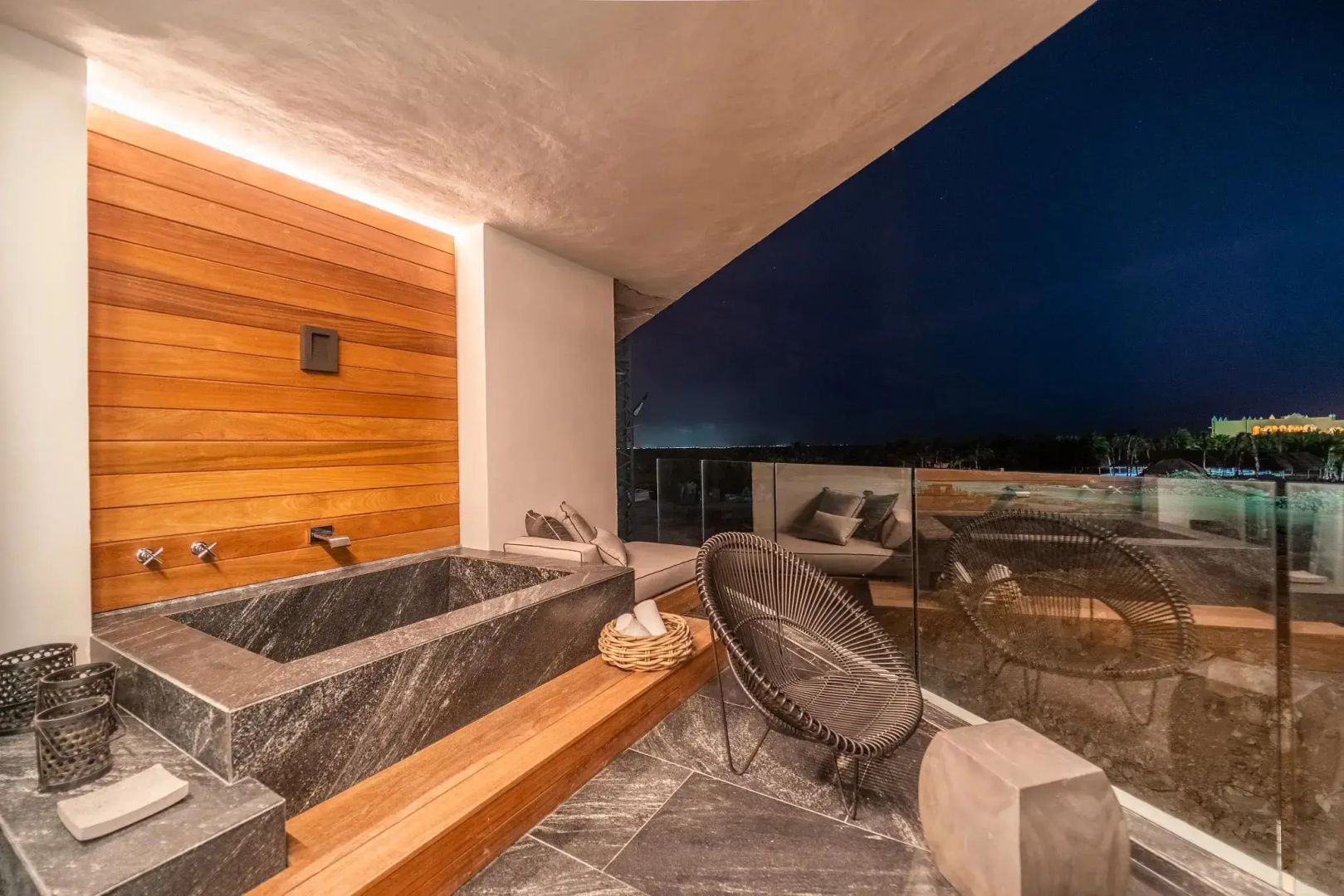 Terrasse bei Nacht mit Wanne aus Stein, Sessel und Blick auf die nächtliche Umgebung.