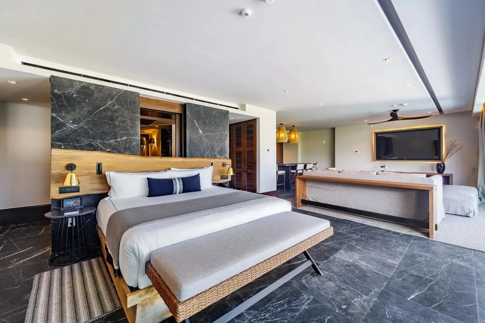Doppelbett mit Holzkopfteil und gepolsterter Bank im geräumigen Hotelzimmer.
