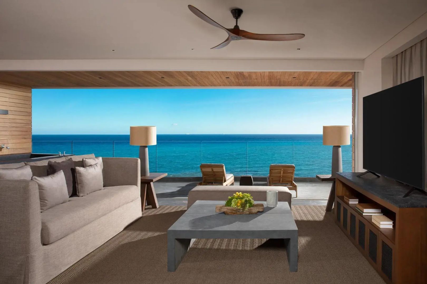 Offener Wohnbereich mit Sofa und Tischen sowie Blick auf eine Terrasse und das blaue Meer.