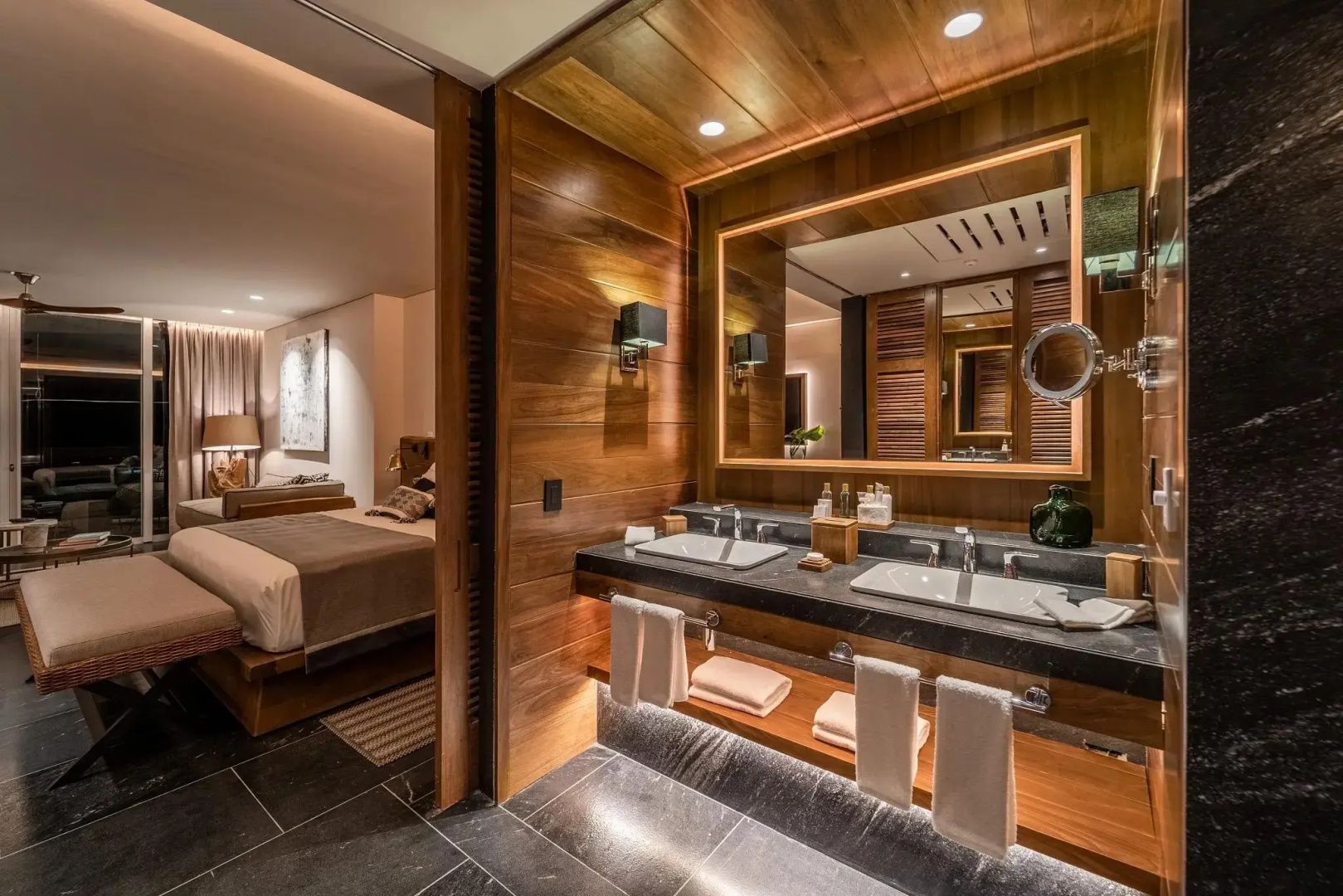 Modernes Badezimmer mit zwei Waschbecken, Beleuchtung und Holzwand im Hotelzimmer.