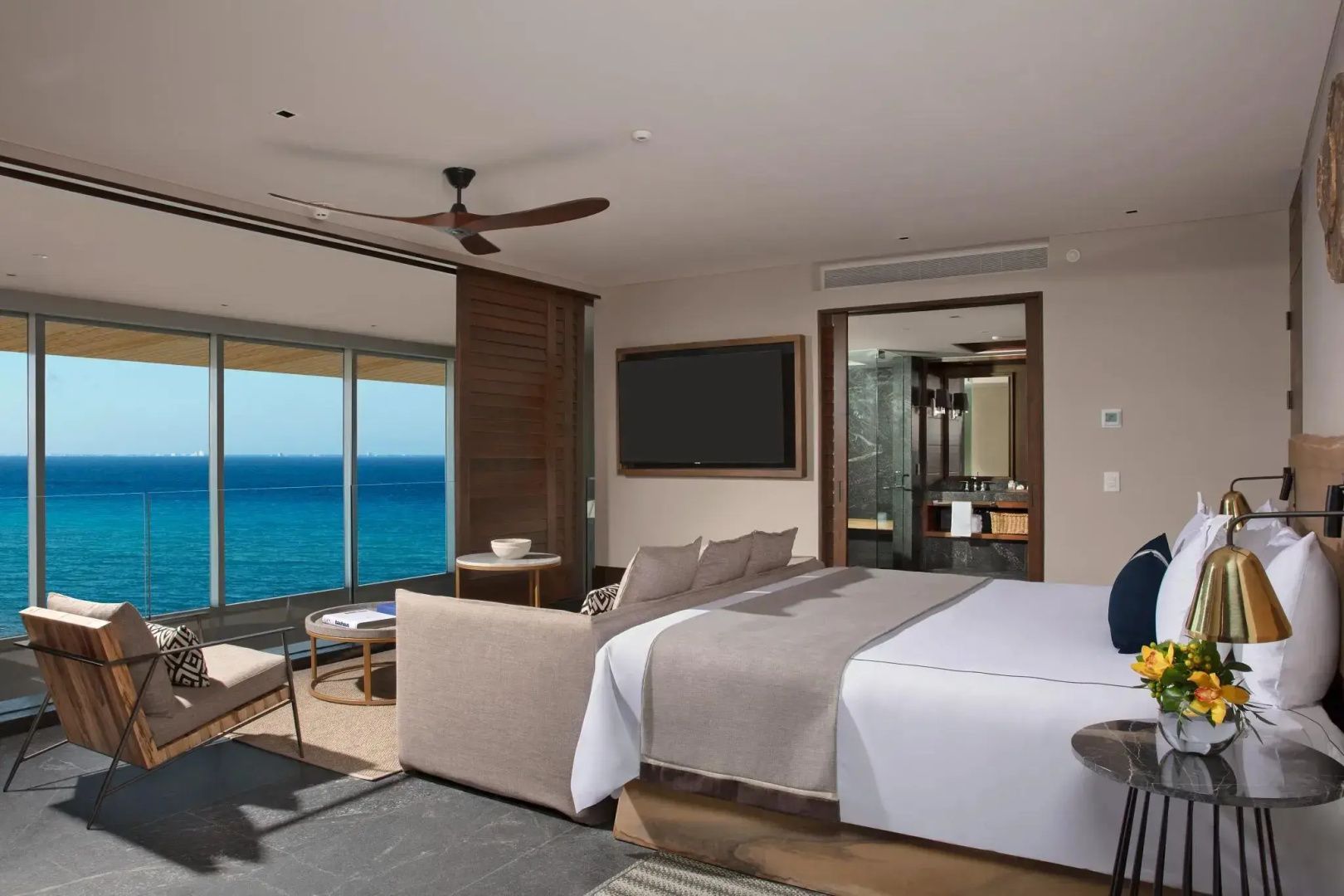 Modernes Hotelzimmer mit großem Doppelbett, Fernseher und freier Sicht auf das blaue Meer.