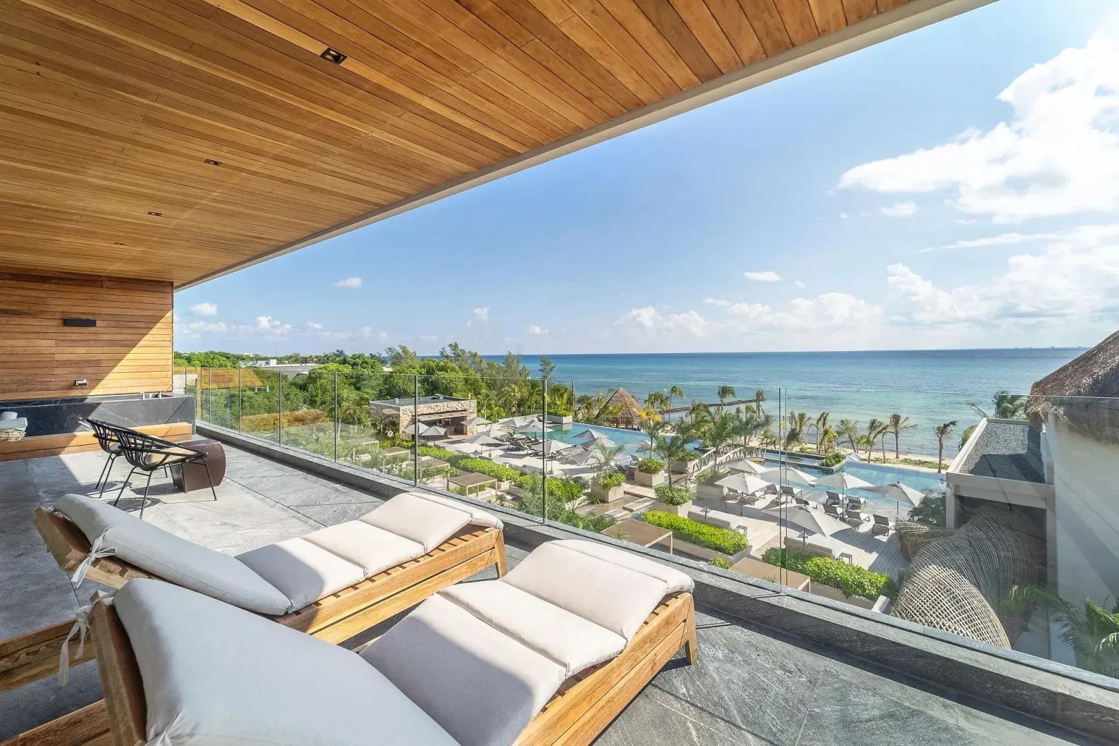 Balkon mit zwei Sonnenliegen und weitem Blick über die Hotelanlage mit Poolbereich und Meer.