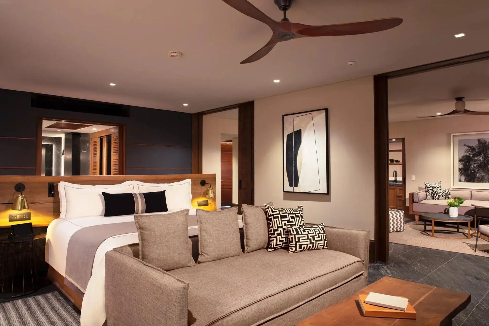Geräumige Hotel-Suite mit Sofa am Fußende des Doppelbetts und Holzdeckenventilator.