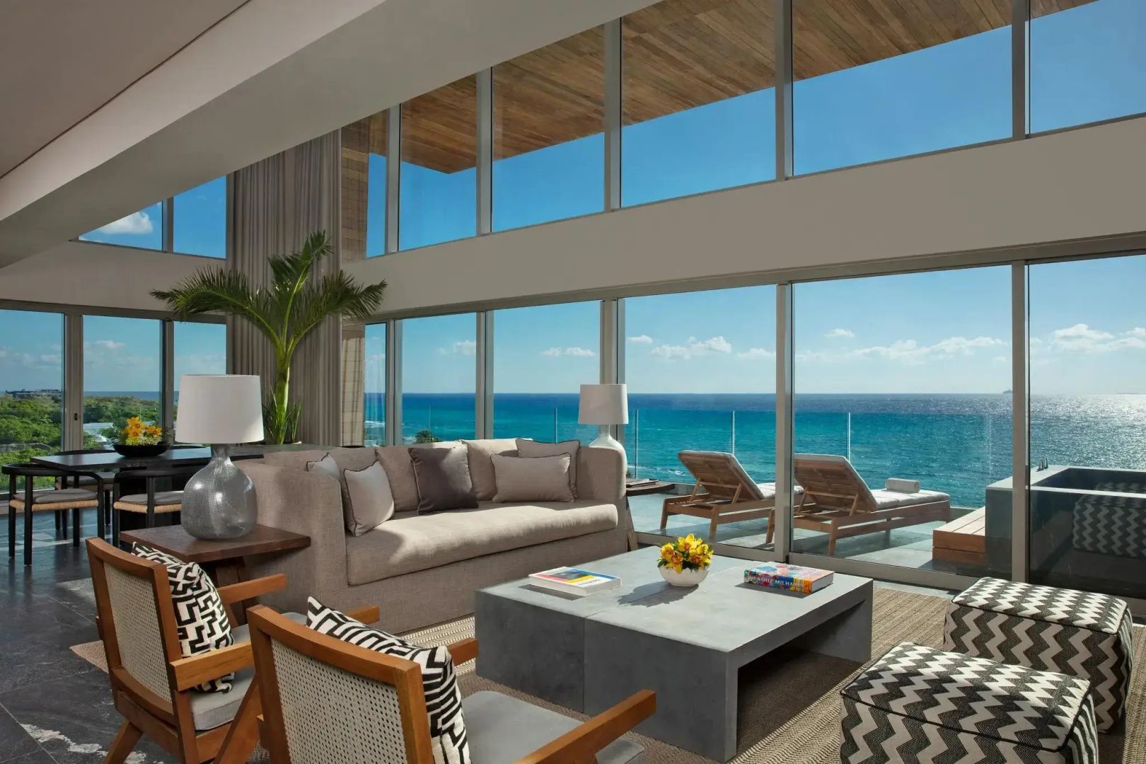 Wohnbereich einer Suite mit heller Sitzgruppe, Couchtisch und hoher Glasfront zum Ozean.
