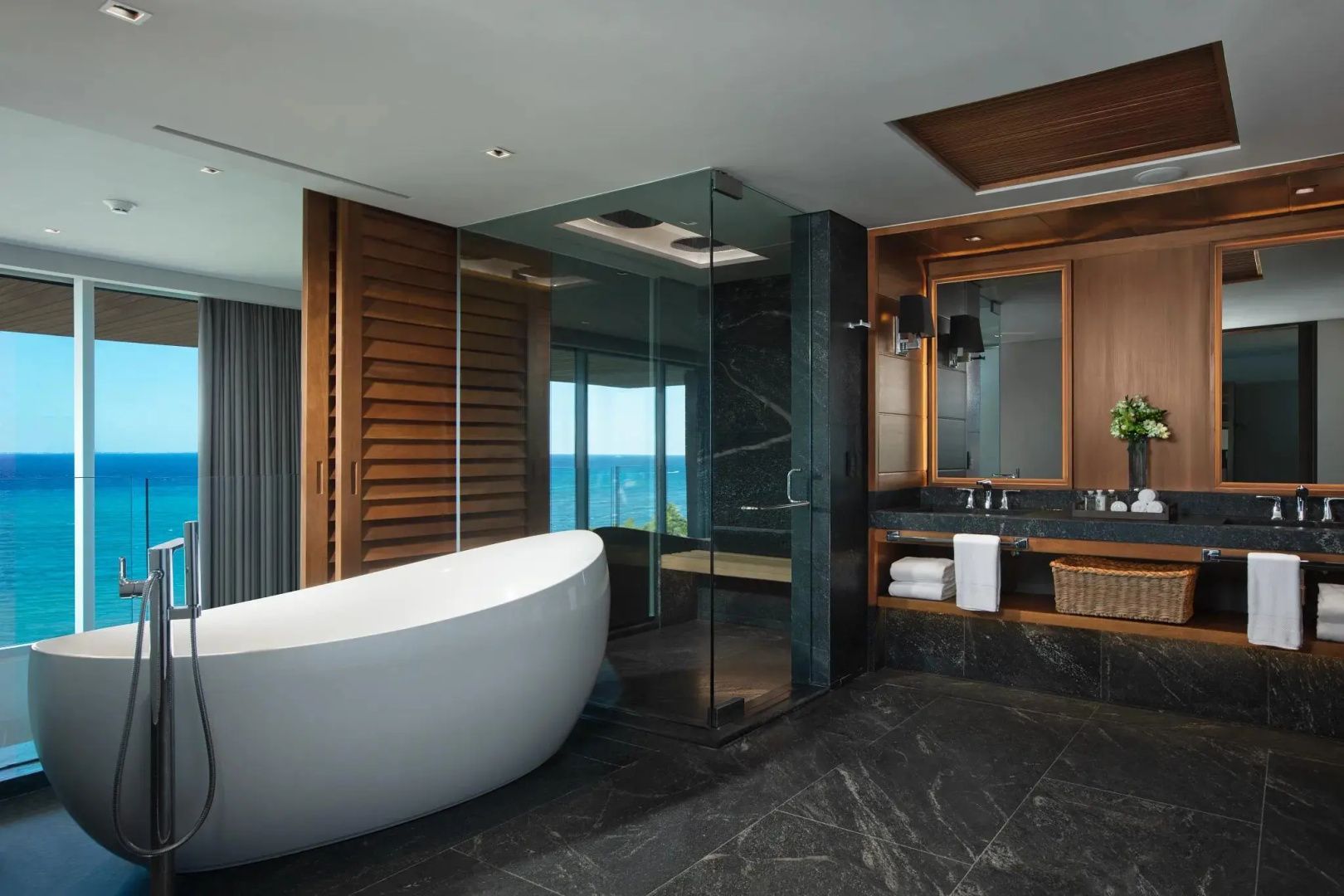 Badezimmer mit freistehender Badewanne, Glasdusche, Waschtisch und Ausblick auf das Meer.