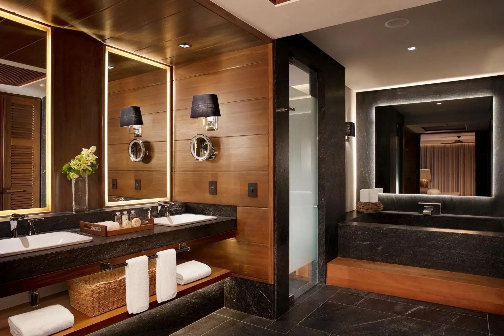 Badezimmer mit beleuchtetem Spiegel, Waschbecken, Handtüchern und einer dunklen Badewanne.