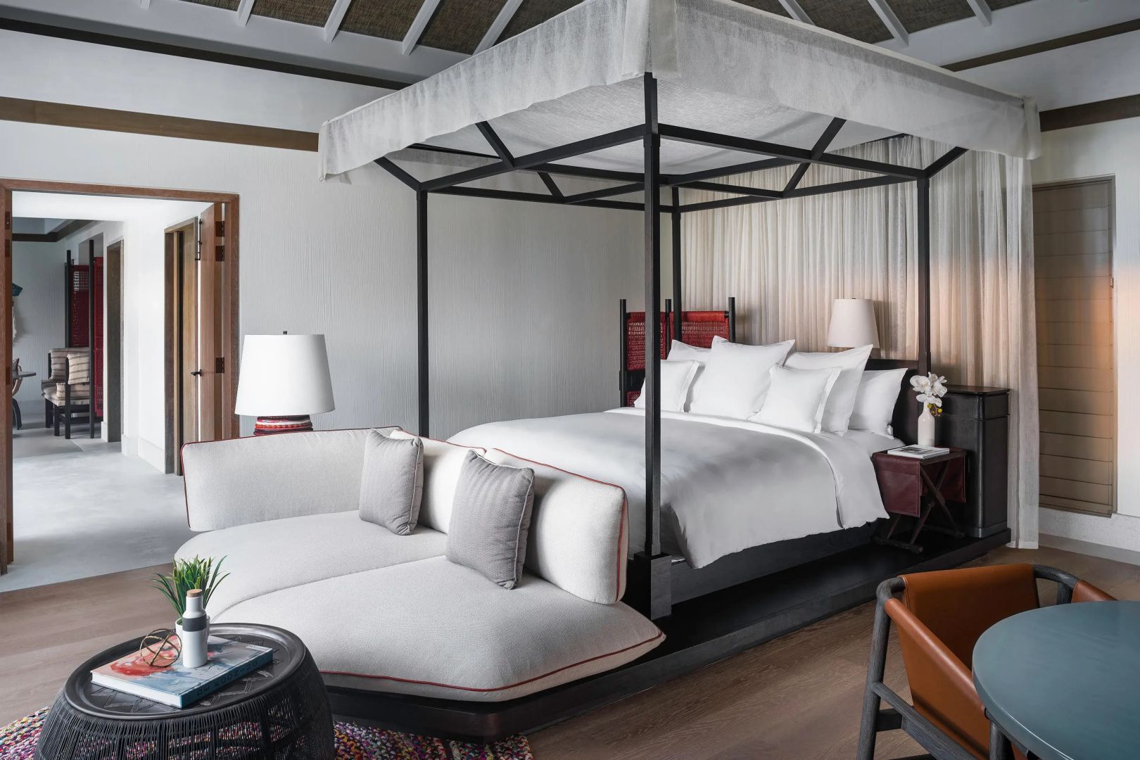 Helles Schlafzimmer mit dunklem Himmelbett, weißer Bettwäsche und geschwungener Couch.