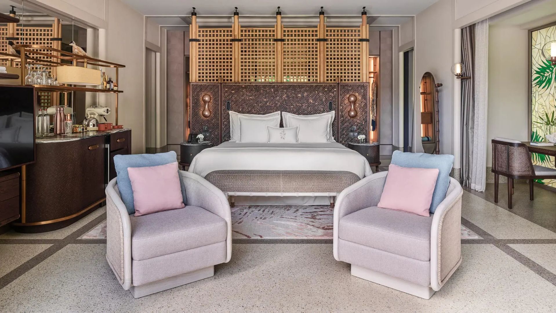 Großes Doppelbett mit weißer Bettwäsche und zwei Sessel im Schlafbereich einer Villa.