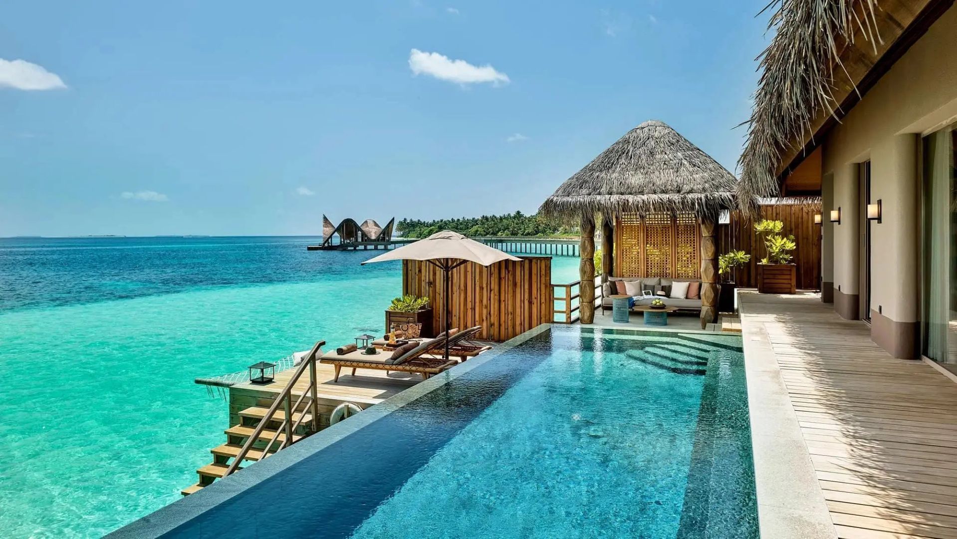 Eigenes Schwimmbecken auf einem Holzdeck über dem Meer mit Sonnenschirm und Pavillon.