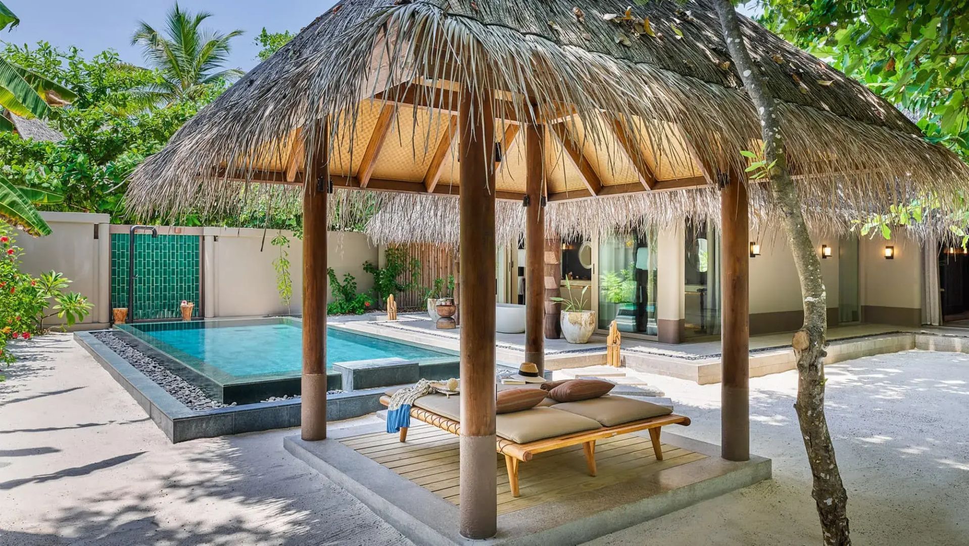 Holzpavillon mit Strohdach, Liegebett und privatem Pool im Außenbereich einer Villa.