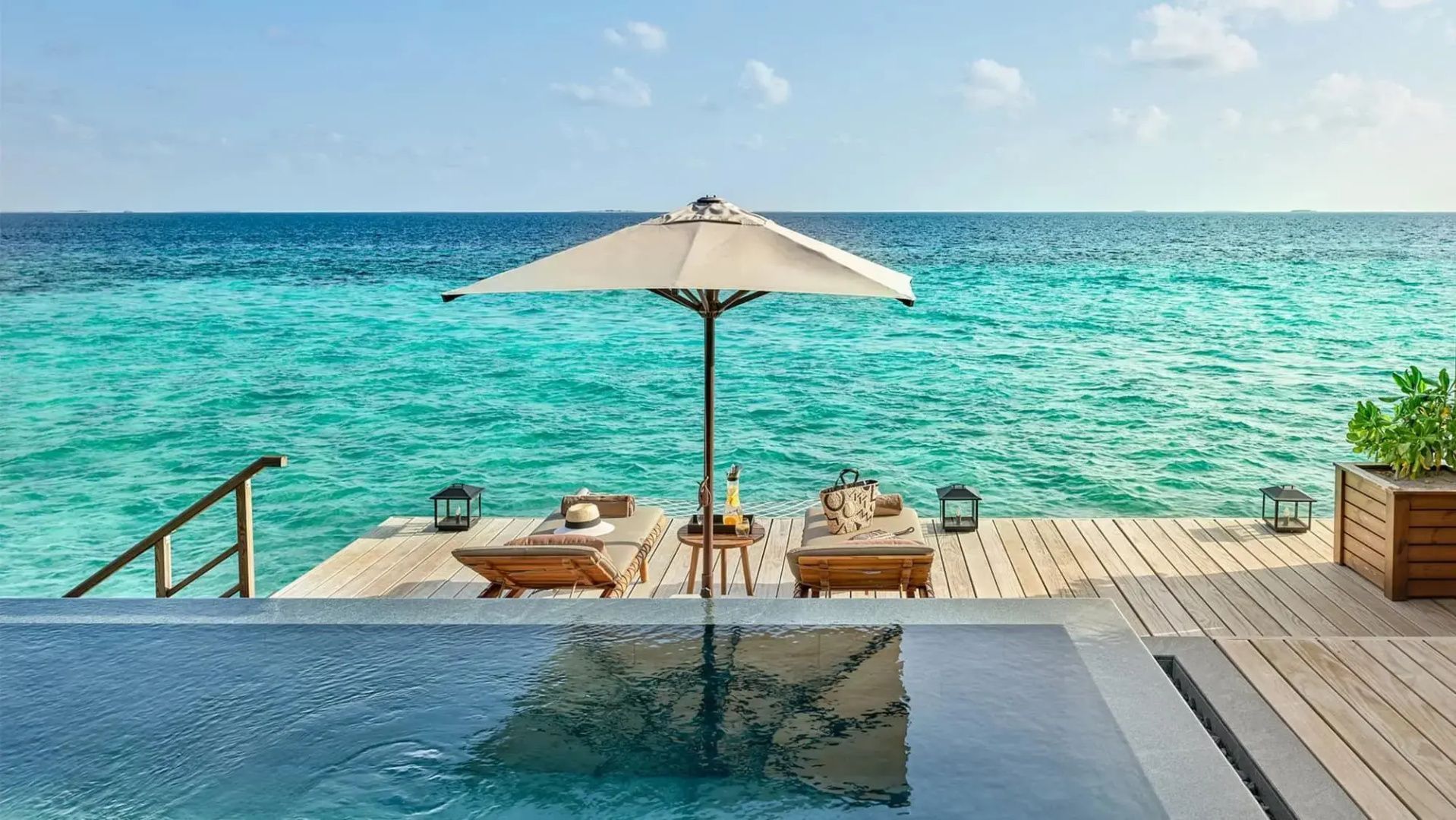 Sonnendeck mit Pool, zwei Sonnenliegen unter einem Sonnenschirm und Blick auf das Meer